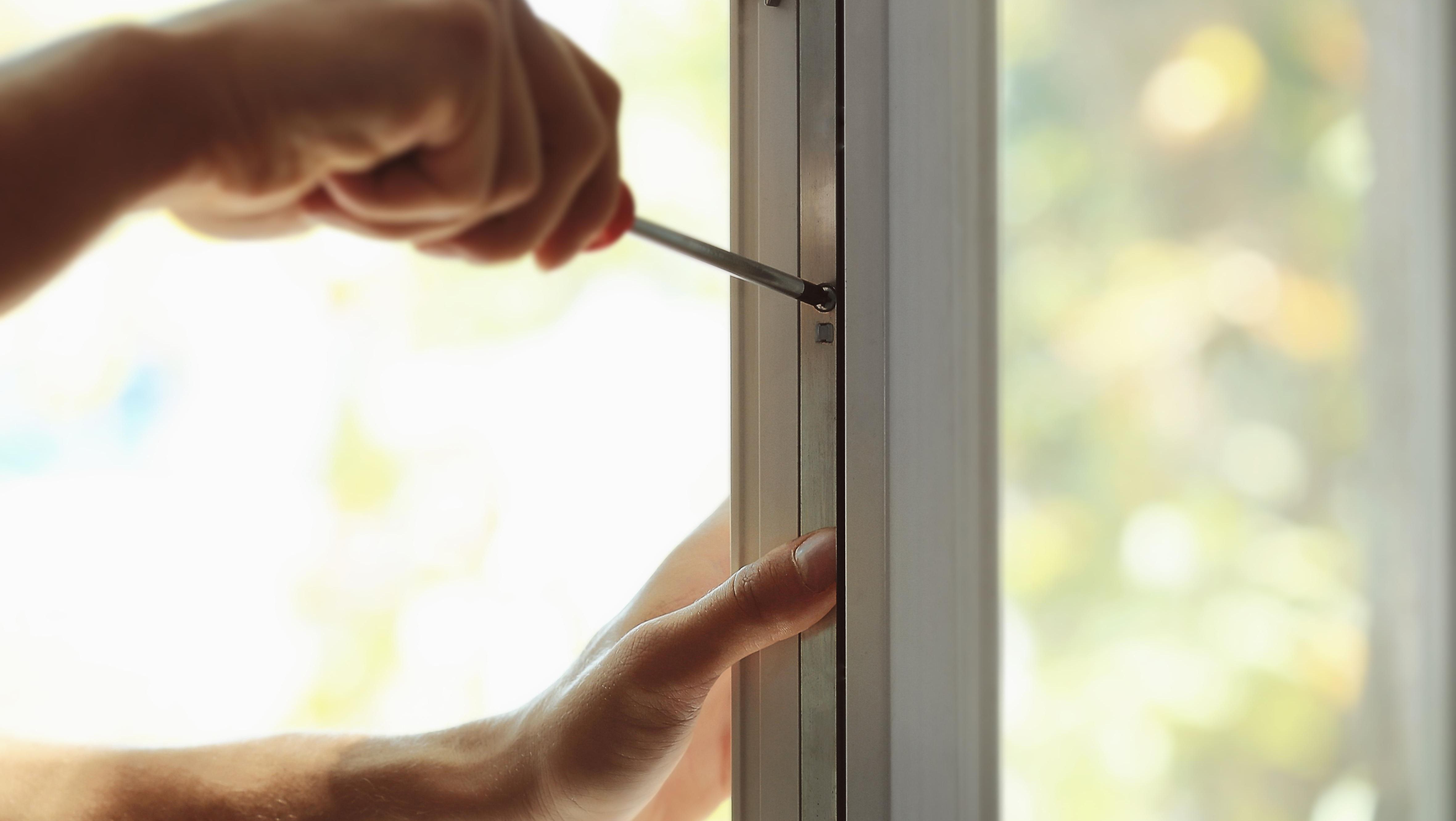 Nærbilde av hender som strammer en skrue i et vindusbeslag