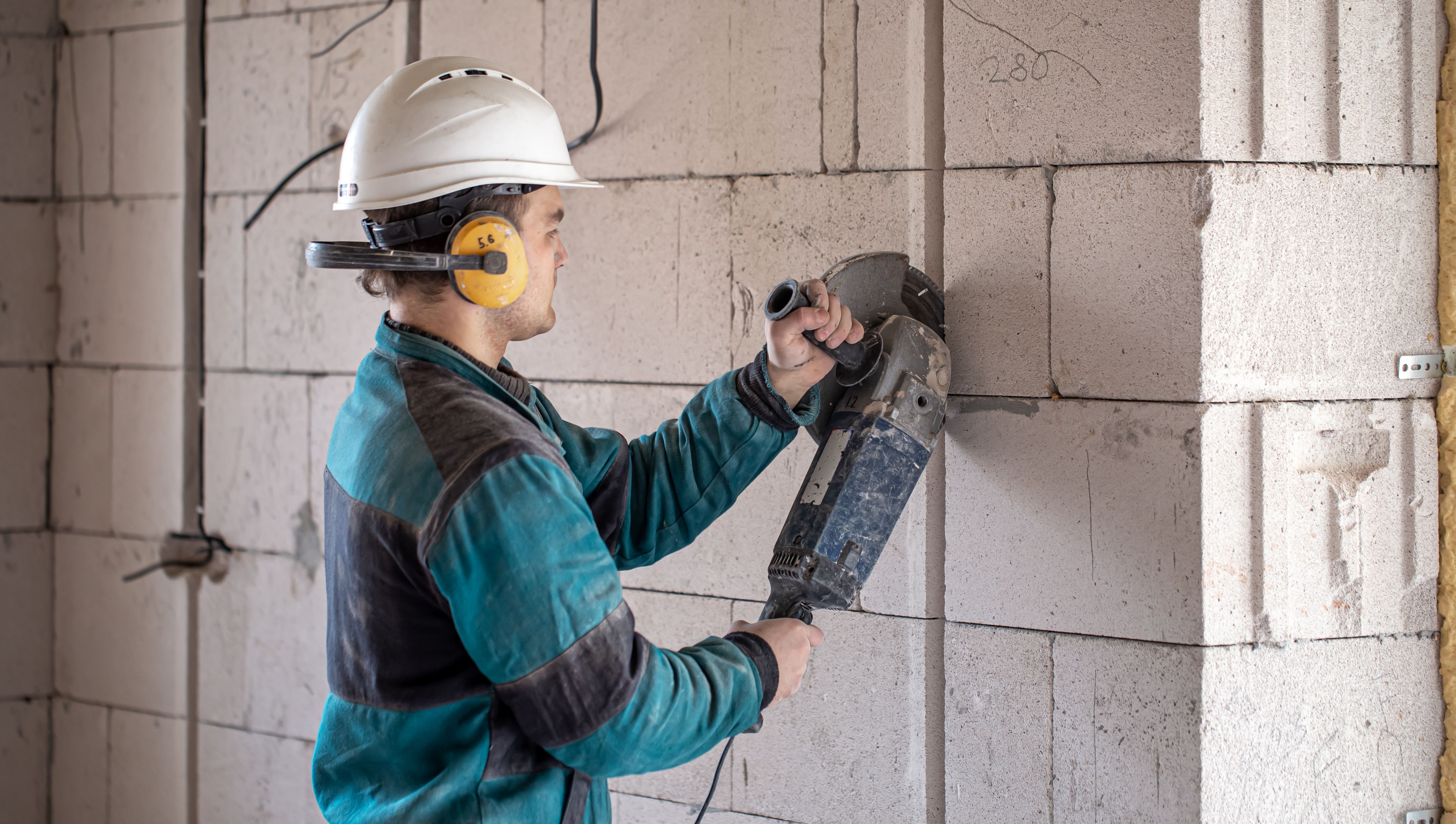 Bygningsarbeider med verneutstyr bruker en vinkelsliper i vegg